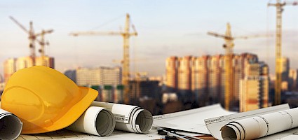 Bautrends: Bauhelm und Pläne vor einer Baustelle
