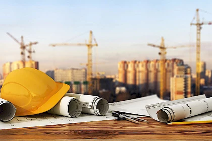 Bautrends: Helm und Baupläne vor einer Baustelle
