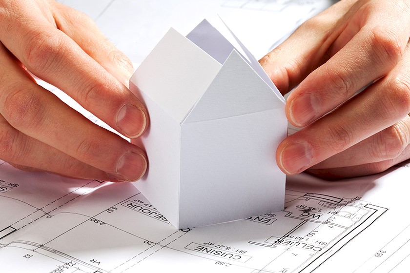 Hände setzen Papierhaus zusammen - Nutzen des Baupreisindex für die Planung
