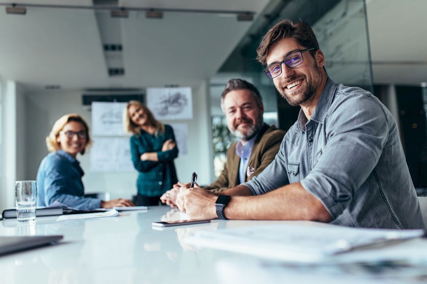 Sales Team sitzt im Besprechungsraum und blickt in die Kamera