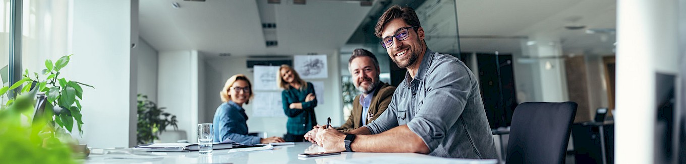 Sales Team sitzt im Besprechungsraum und lächelt in die Kamera