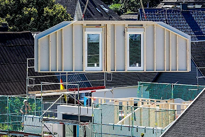 Modulbauweise: Hauswand in Fertigbauweise wird mit Kran in Position gebracht.