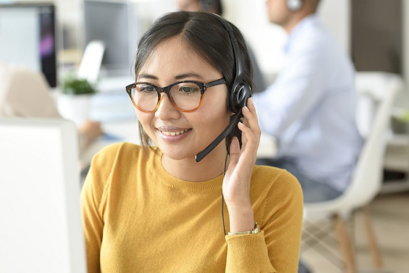 Mitarbeiterin im Kundenservice telefoniert lächelnd mit Kund:innen