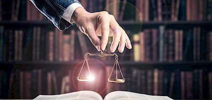 Vergabetransformationspaket: Hand hält Waage über Gesetzesbuch