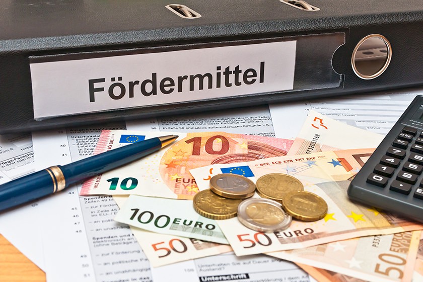 Order mit "Fördermittel" Aufschrift, daneben Geld und Dokumente